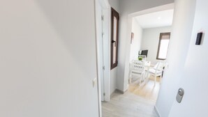 A hallway leading to a dining area with white furniture and a small table with a plant.