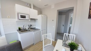 A modern kitchen with white cabinets, a microwave, and a dishwasher. There is a dining area with a table, chairs, and a remote control.