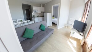 Una sala de estar moderna con un sofá gris, dos cojines verdes, un televisor de pantalla plana y piso de madera.