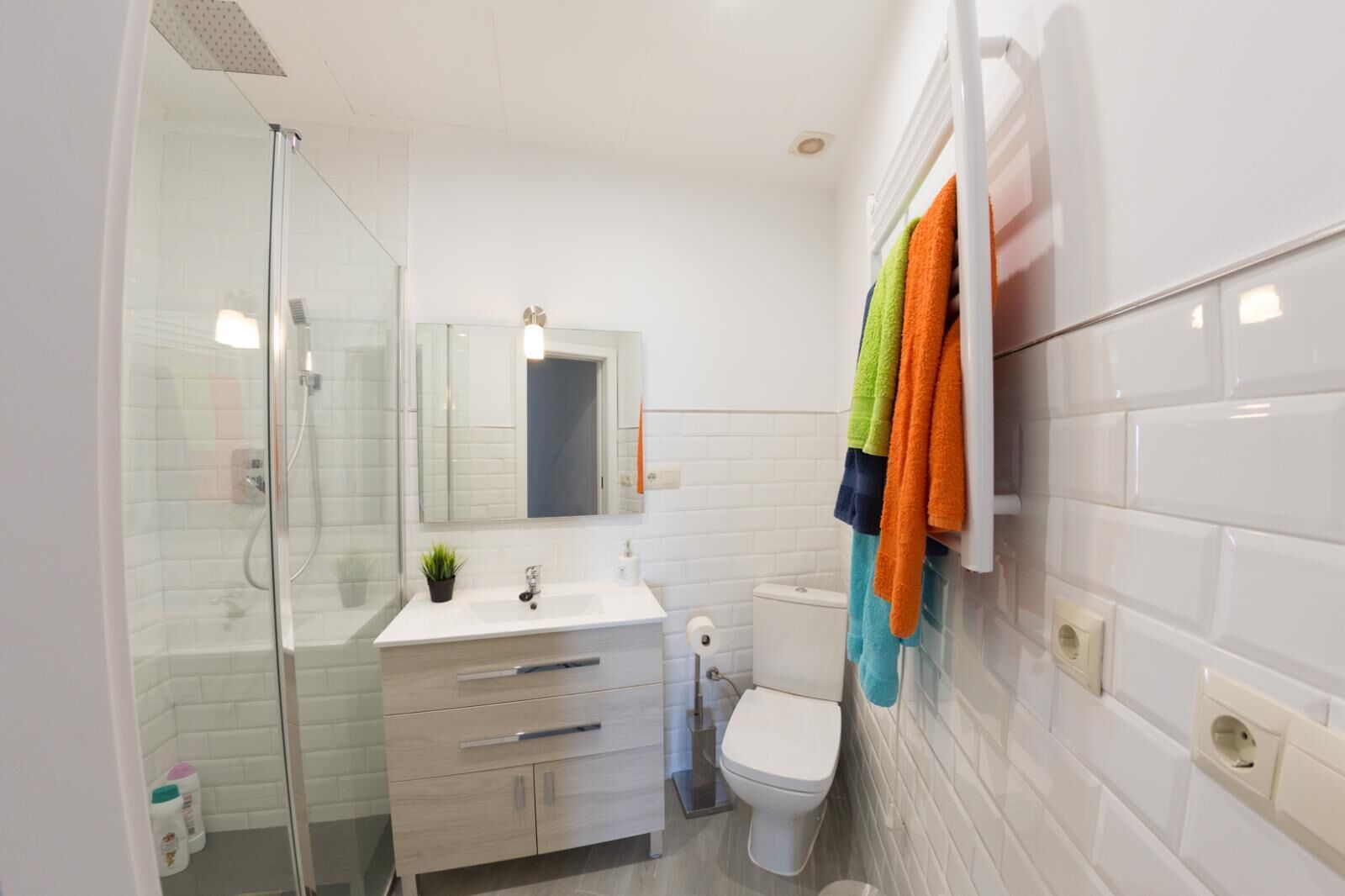 Un baño moderno con cabina de ducha de vidrio, un lavabo blanco con espejo y un inodoro.