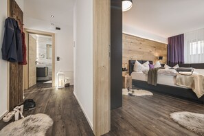 Ett modernt hotellrum med en väggpanel i trä, en säng med många kuddar, ett nattduksbord, en lampa och utsikt över badrummet.
