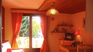 Una stanza accogliente con soffitto in legno, un tavolo con sedie, una televisione e una finestra con tende.