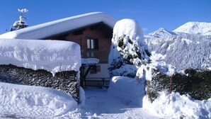 Un chalet imbiancato dalla neve, con facciata in legno, un camino e un cielo azzurro limpido sullo sfondo.