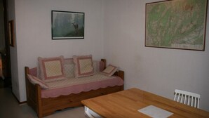 A small room with a wooden sofa, a dining table, and two framed pictures on the walls. - Studio Le Colombier N ° 18 (Aillon-le-Jeune)