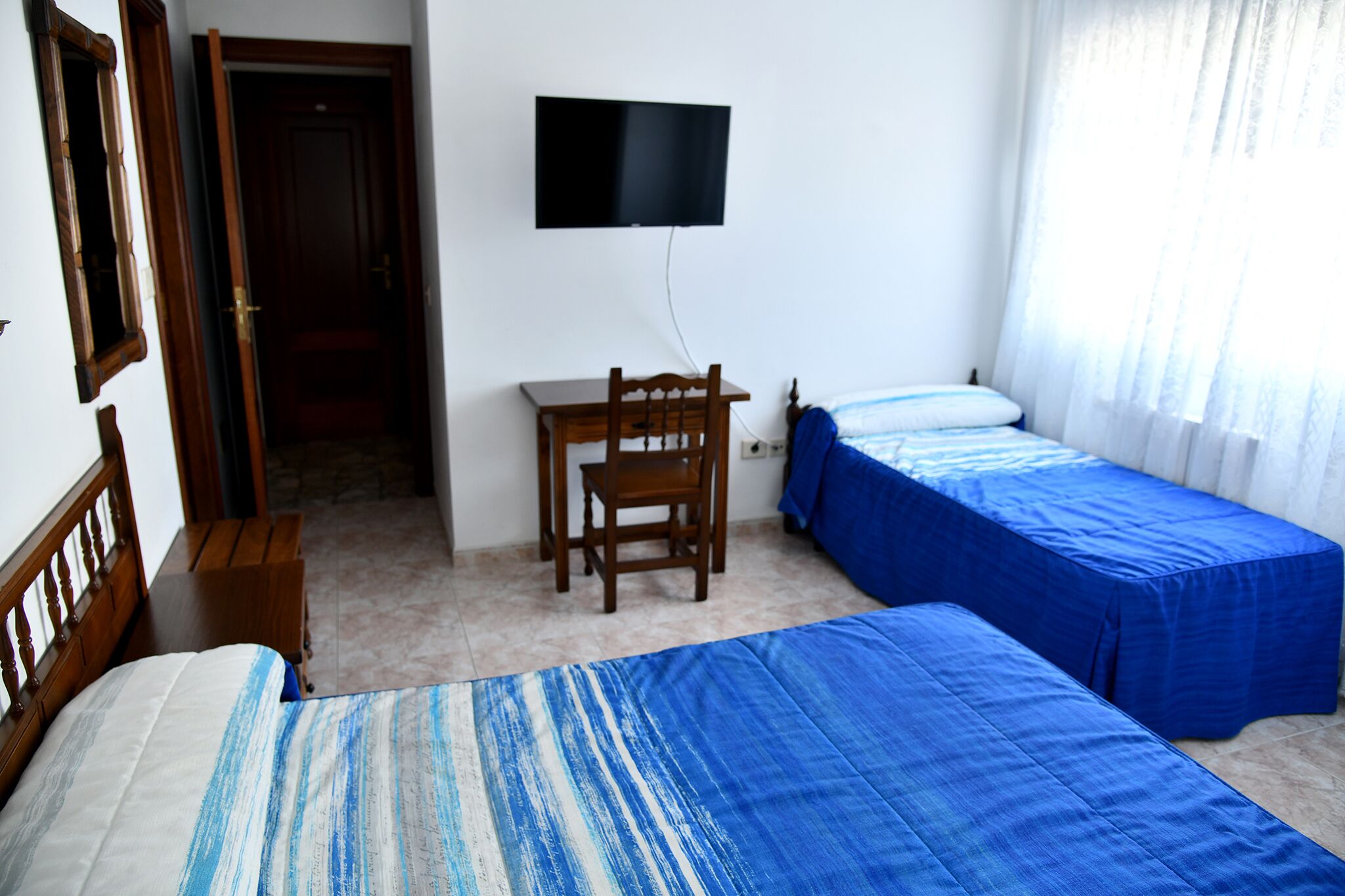 Ein Zimmer mit zwei Betten, einem Schreibtisch, einem Stuhl und einem Fernseher.