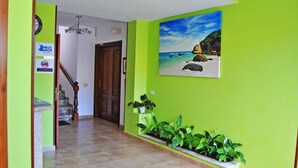Un pasillo con paredes verdes, una escalera de madera y un cuadro que representa una escena de playa.