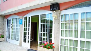 Un edificio con un amplio acceso de puerta de vidrio, un letrero azul con la letra 'H' y una jardinera con flores rojas.