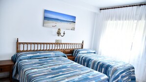 Un dormitorio con dos camas, una mesita de noche, una lámpara de pared y vista al mar.