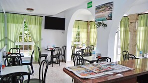 Comedor con mesas y sillas, un televisor en la pared y un cartel con el número de la habitación.