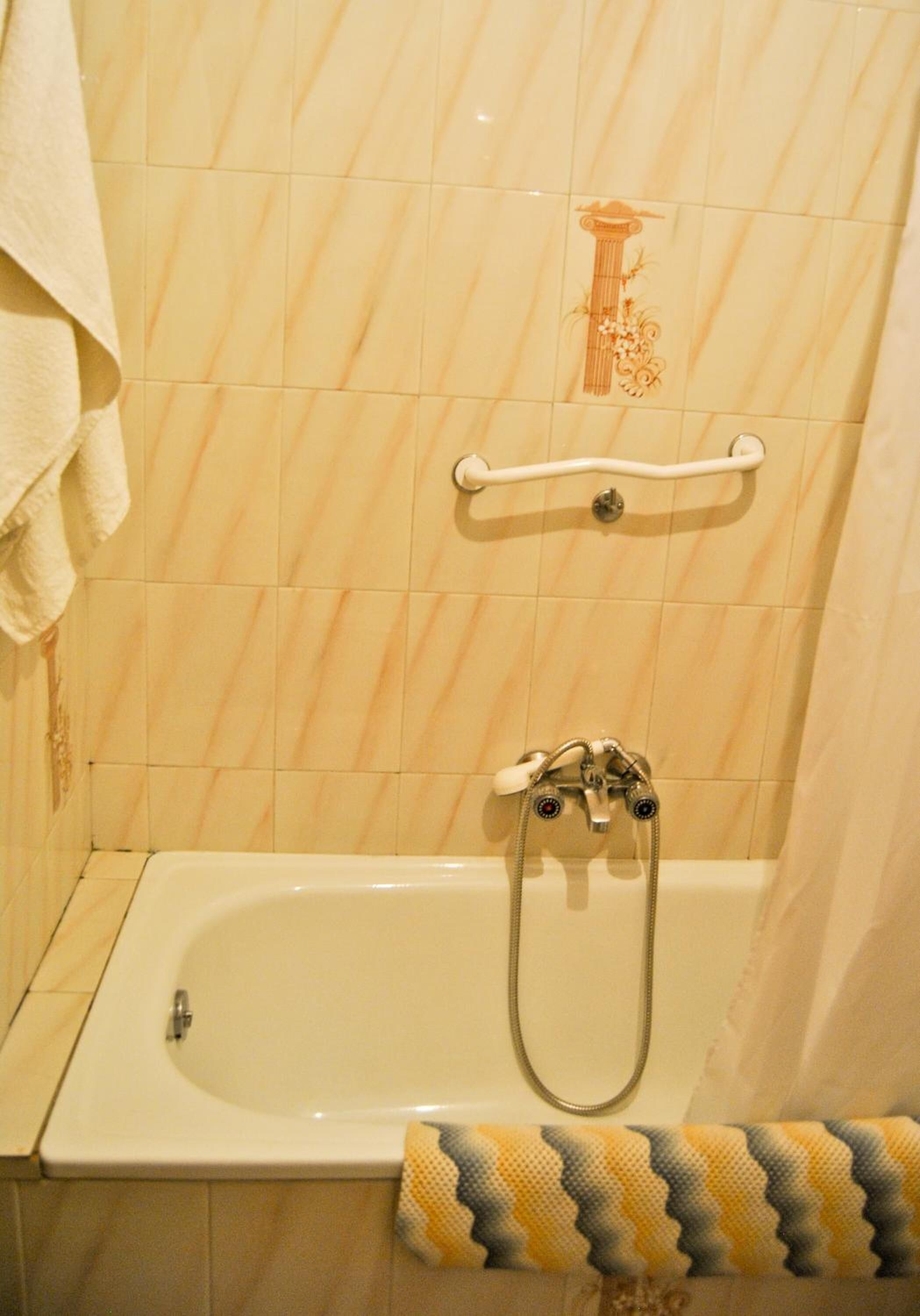 A bathroom with a bathtub, a towel rack, and a decorative tile design on the wall.