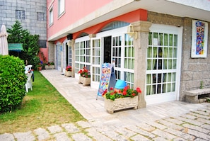 A building with a red facade, multiple windows, and outdoor seating areas with planters and umbrellas. - Hotel Maruxa (Sanxenxo)