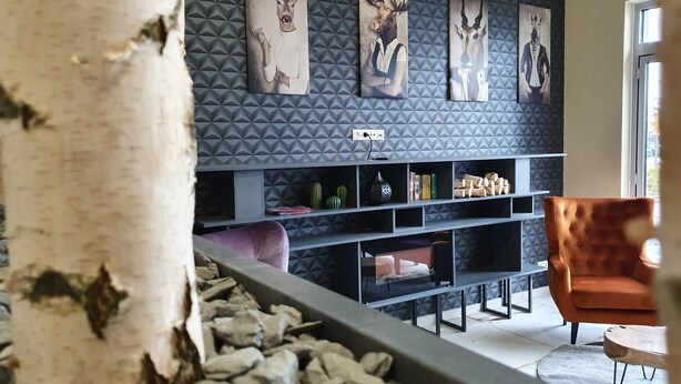 Una sala de estar moderna con un muro de patrón geométrico, un tronco de árbol grande, un jardín de rocas y un sillón rojo.