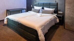 Una cama bien tendida con cabecera oscura y ropa de cama blanca, una mesita de noche y un enchufe en la pared.