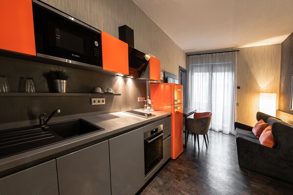 A modern kitchen with a Bosch microwave, a sink, and a refrigerator. There is a dining area with a table and chairs. - Hotel Lifestyle Mindelheim (Mindelheim)