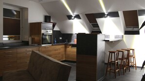 Une cuisine moderne avec des meubles en bois, un four encastré et un réfrigérateur. On y trouve des tabourets de bar et une fenêtre donnant sur l’extérieur.