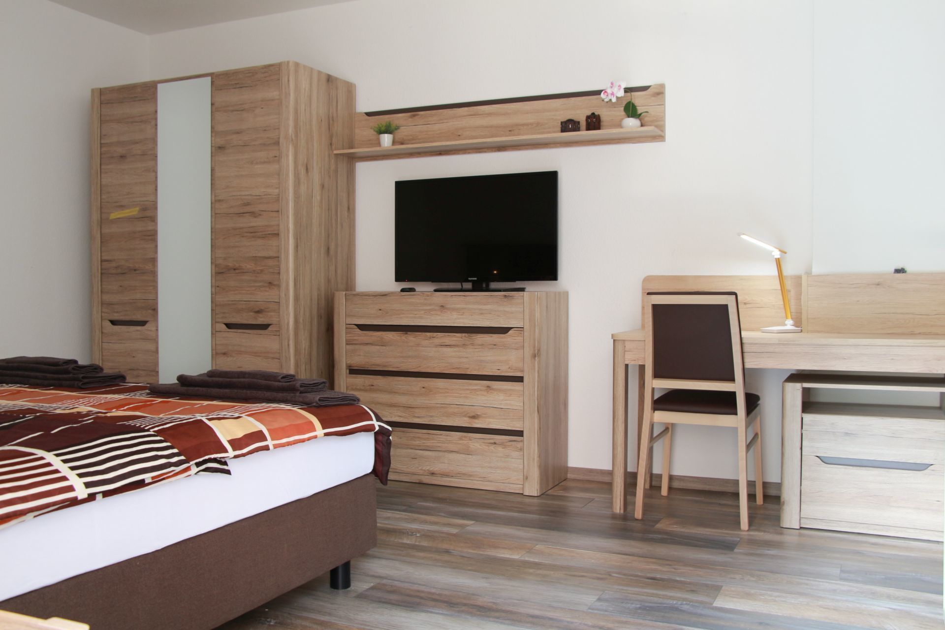 A bedroom with a bed, a TV, a desk, and a chair.
