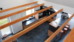 Une cuisine moderne dotée d’un îlot central, de poutres en bois et offrant une vue sur l’extérieur.