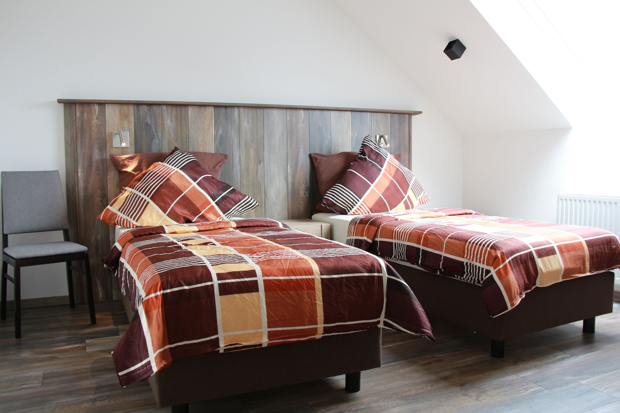 A bedroom with two beds, a wooden headboard, a chair, and a window.