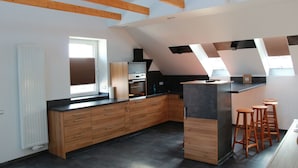 Une cuisine moderne avec des meubles en bois, un îlot central et un plafond en pente avec des poutres apparentes.