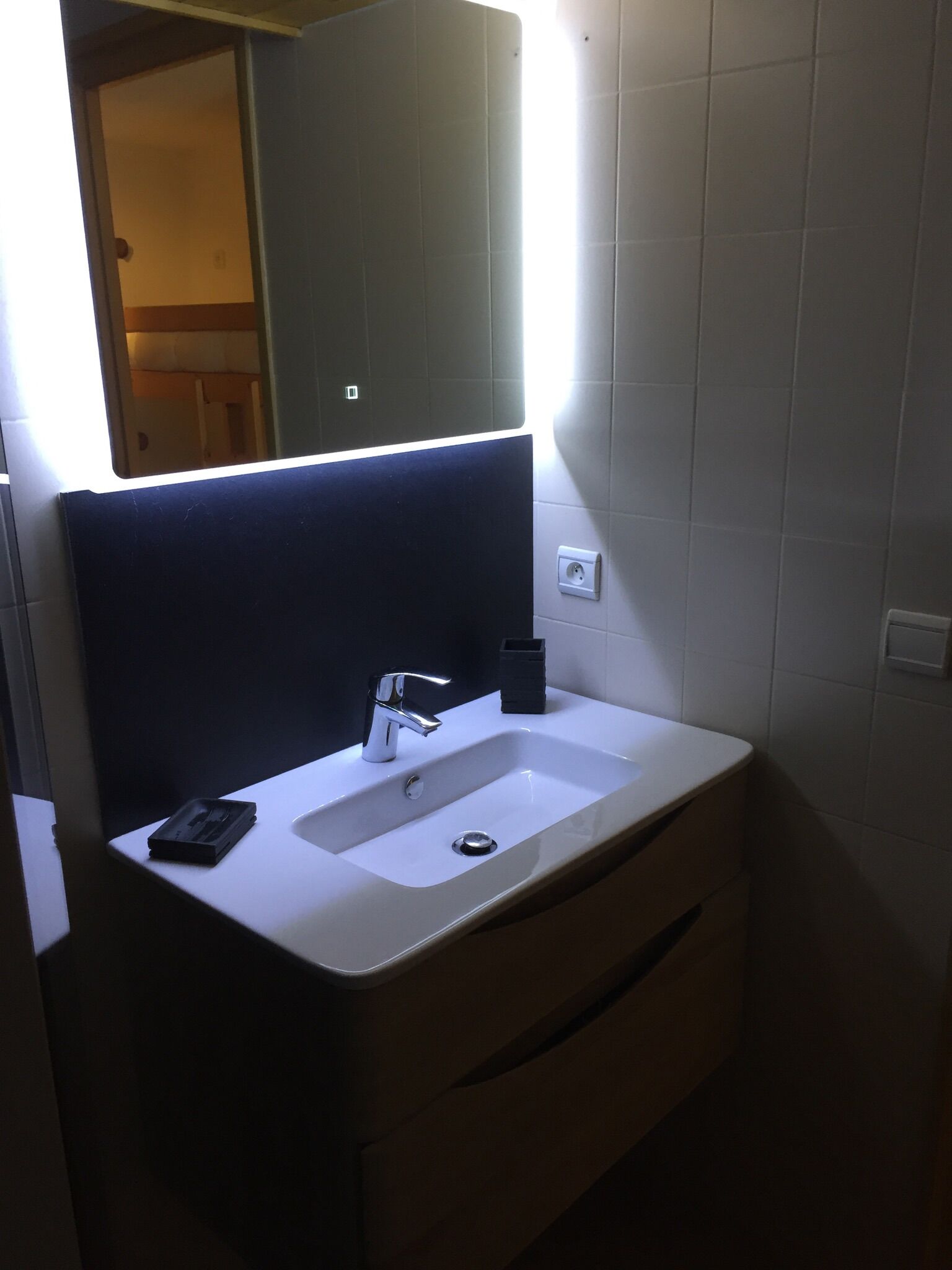 A bathroom with a white sink, a mirror with a black frame, and a light above the mirror.