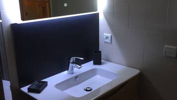 A bathroom with a white sink, a mirror with a black frame, and a light above the mirror.