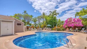 A swimming pool with a curved edge, surrounded by lounge chairs and umbrellas, with palm trees and flowering plants in the background. - Traveler Favorite! Spacious, comfortable, updated 5-STAR Wailea Retreat. 🏝  (Wailea)