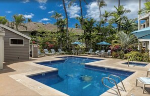 A pool area with lounge chairs and umbrellas, surrounded by palm trees and a clear sky.