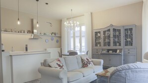 Una sala de estar con un sofá, un aparador con puertas de cristal y una zona de cocina con mostrador y lámparas colgantes.