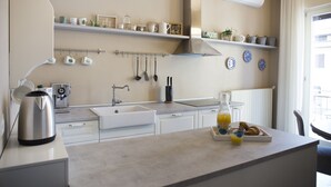 Una cocina moderna con armarios blancos, una cafetera, un hervidor y una bandeja de desayuno con cruasanes y jugo.