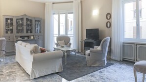 Una sala de estar con un sofá, sillones, un televisor, un mueble con puertas de vidrio y un ventanal grande.