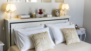 Una cama bien hecha con almohadas blancas y estampadas, una mesita de noche con lámpara y un reloj.