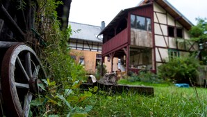 A traditional house with a wooden wheel, surrounded by greenery.