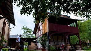 A rustic two-story building with a wooden exterior, a covered porch, and a stone fireplace.