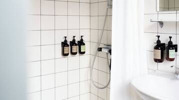 Un baño con azulejos blancos, ducha, lavabo y dos botellas de champú en la pared.