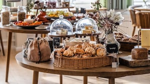 A buffet table with various food items, including breads, cheeses, and a decorative vase with flowers. - Hotel Siemsens Gaard (Svaneke)