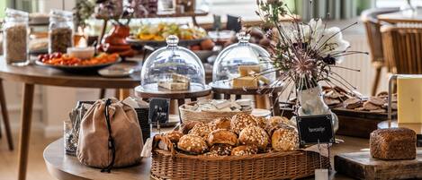 A buffet table with various food items, including breads, cheeses, and a decorative vase with flowers.