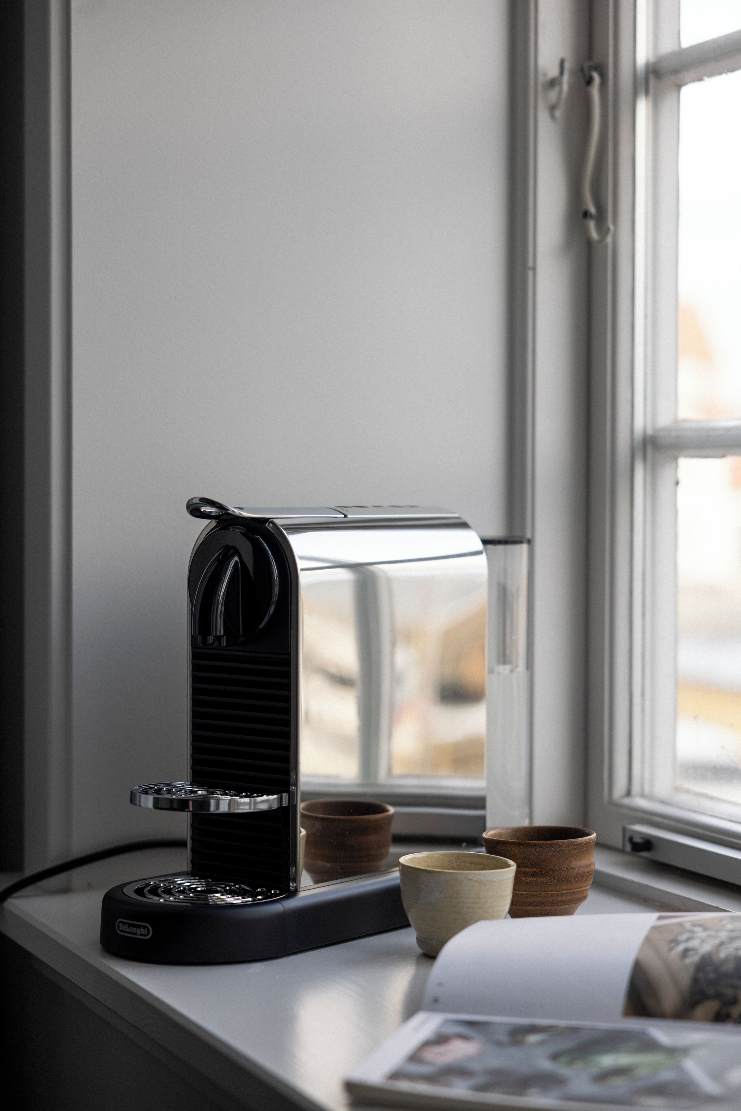 Una cafetera en un alféizar con vistas al exterior.