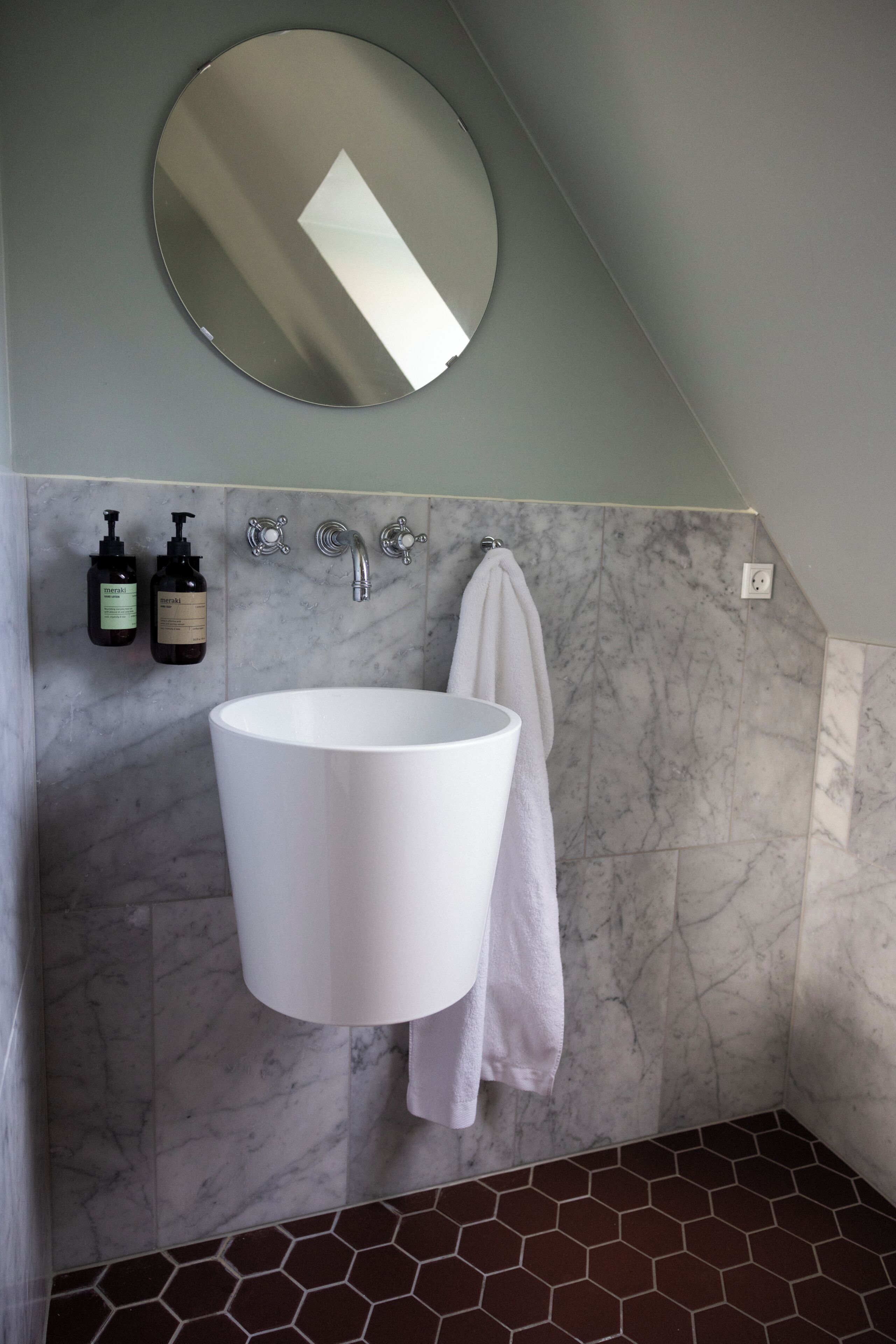 Une salle de bain avec un lavabo blanc, un miroir rond et deux bouteilles de shampoing.