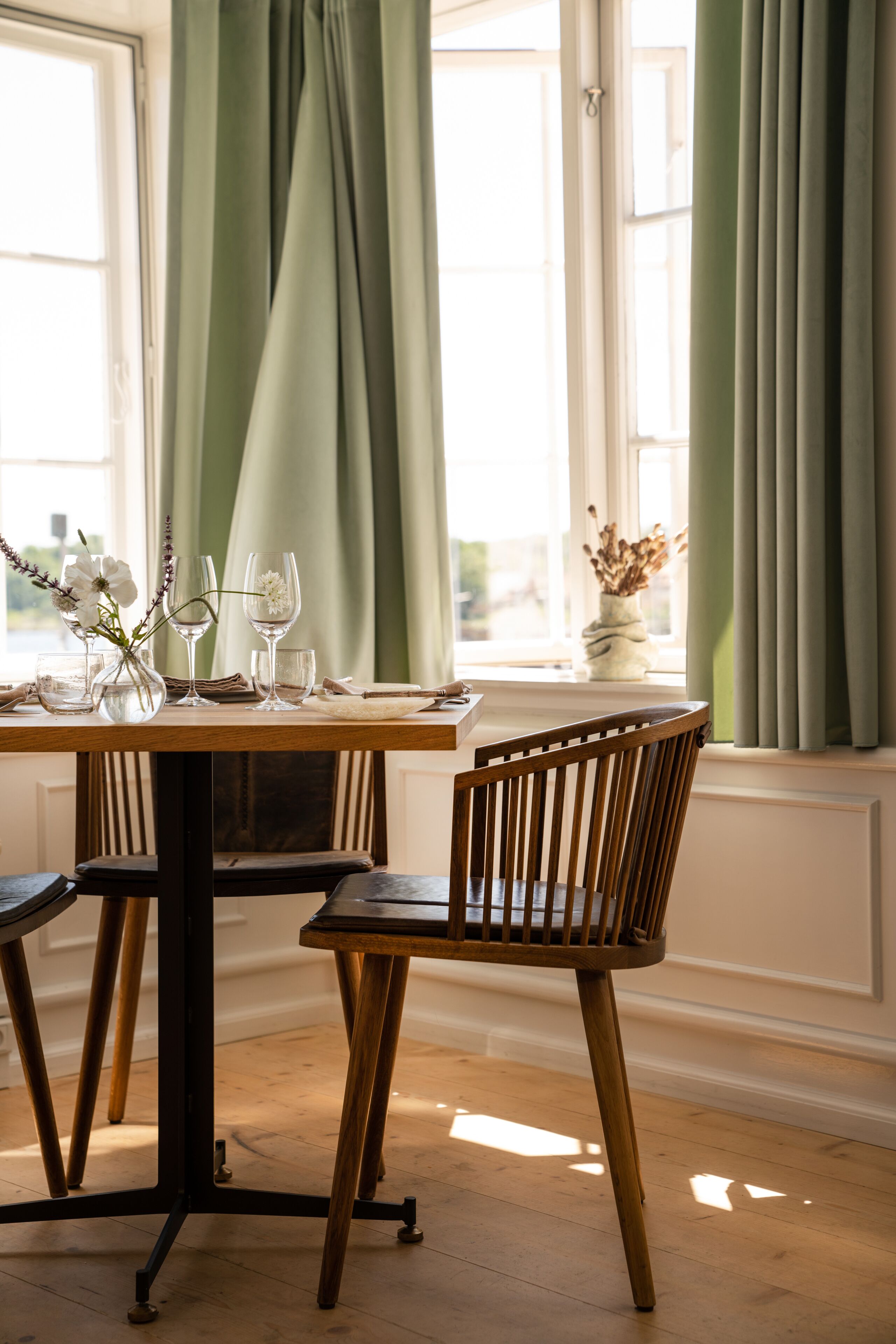 Une table à manger dressée avec de la verrerie et un vase de fleurs, accompagnée d’une chaise en bois.