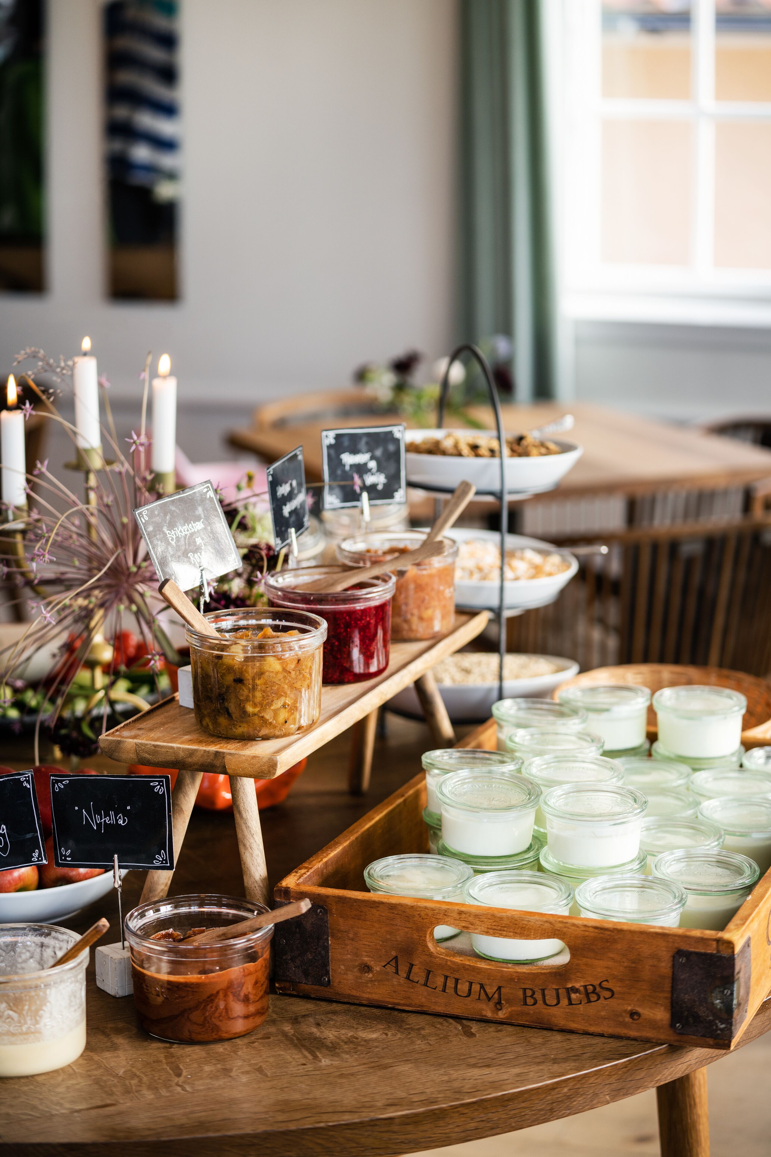Une table de buffet proposant divers plats et accompagnements, notamment des pots de tartinades et un plateau en bois portant l’inscription « ALLIUM BUTTS ».