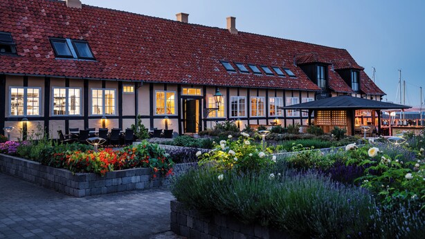 A traditional building with a tiled roof, multiple windows, and a well-maintained garden with various plants and flowers. - Hotel Siemsens Gaard (Svaneke)