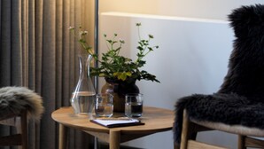 A room with a wooden table, a lamp, a chair, a vase with flowers, and a window with curtains. - Hotel Siemsens Gaard (Svaneke)