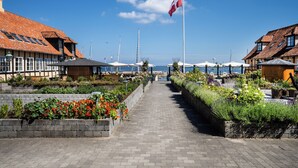 A seaside walkway with a flag, buildings, and a view of the sea. - Hotel Siemsens Gaard (Svaneke)