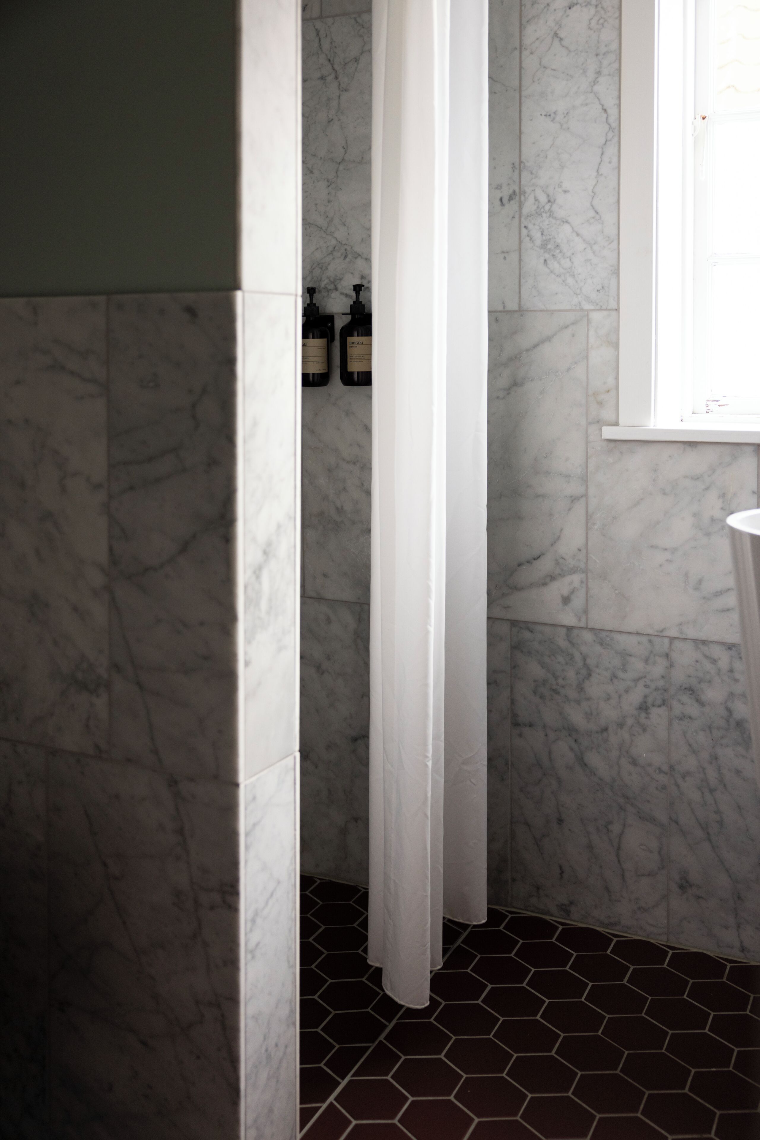 A bathroom with marble walls, a white door, and a hexagonal tile floor.