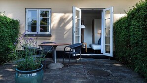 An outdoor seating area with a table and chairs, a potted plant, and a door leading to an interior space. - Hotel Siemsens Gaard (Svaneke)