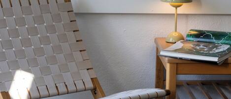Una habitación con una silla tejida, una mesita con una lámpara y un cuadro abstracto enmarcado en la pared.