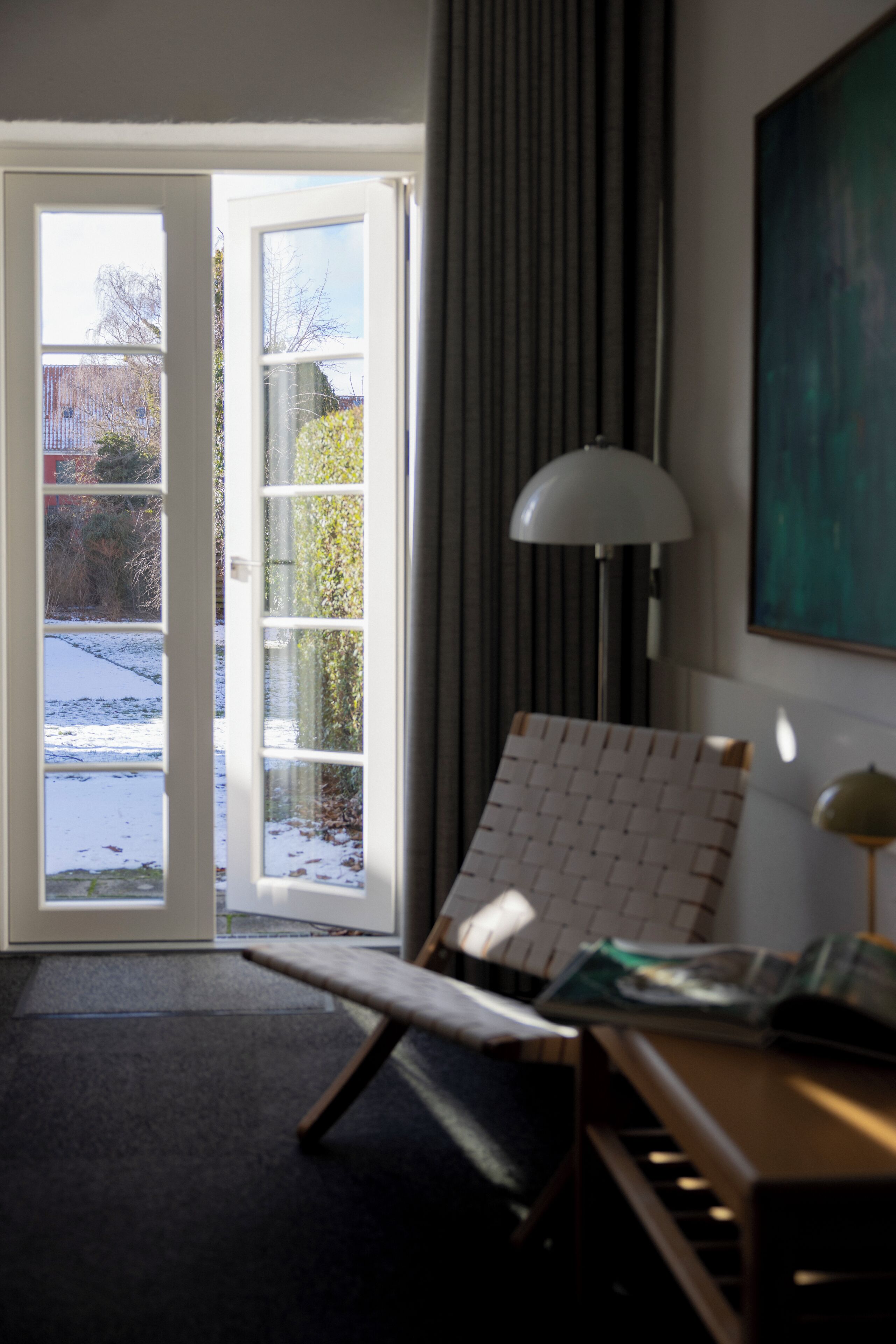 A room with a large window, a chair, a lamp, and a painting on the wall.