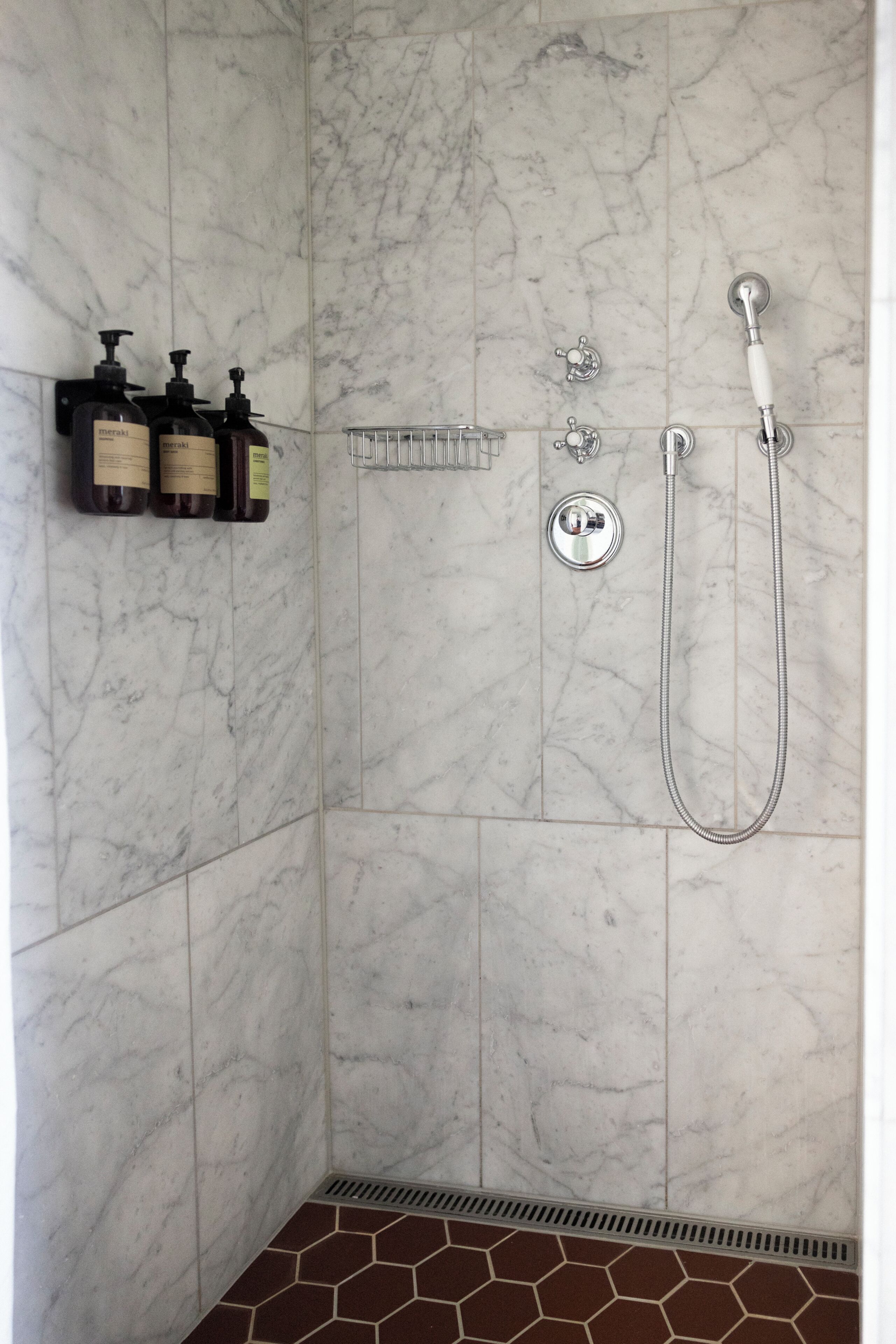A bathroom with a shower, a hand dryer, and a shelf with toiletries.