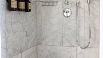 A bathroom with a shower, a hand dryer, and a shelf with toiletries.