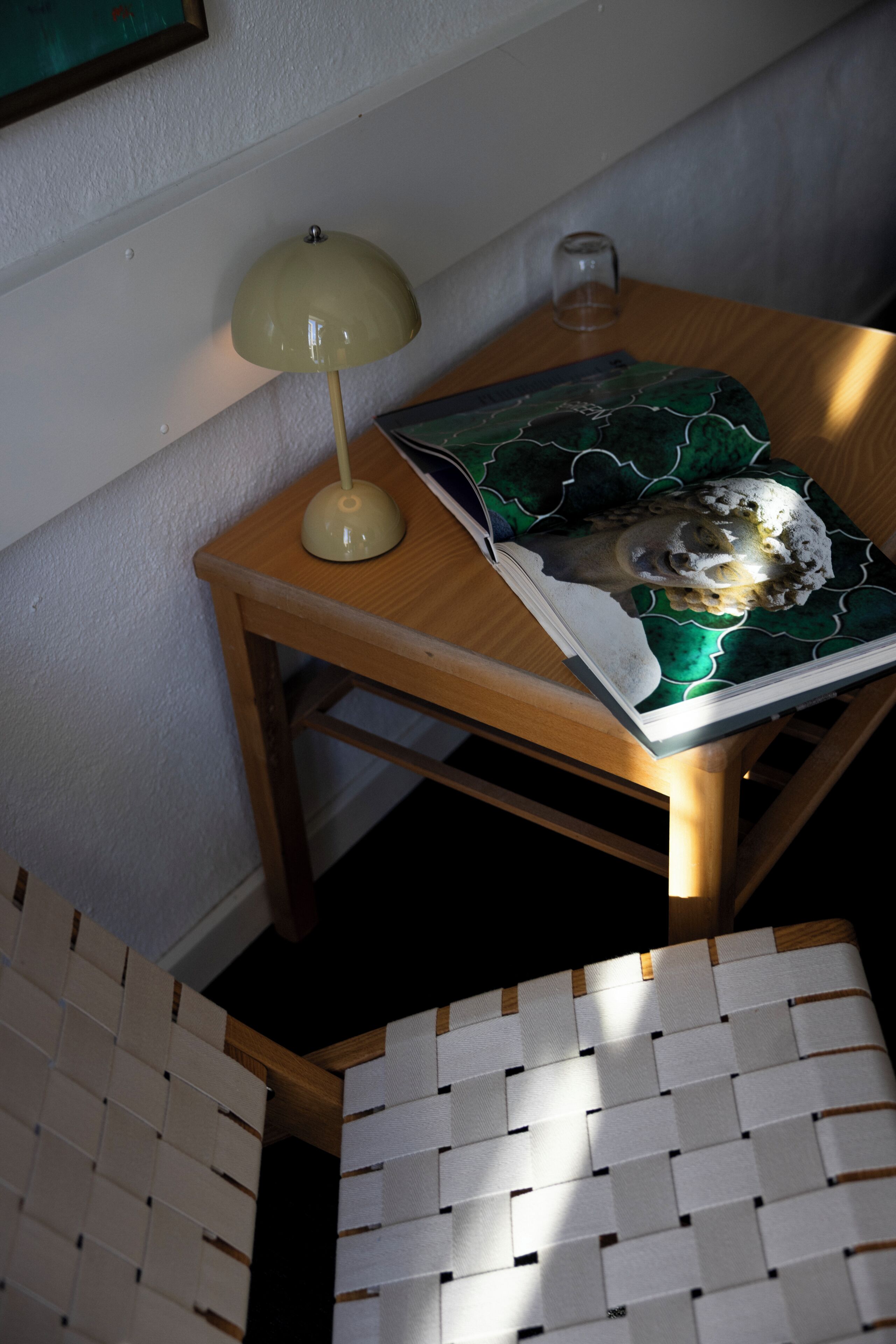 A wooden table with a lamp, a glass, and a book with a green cover.